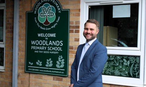 New headteacher, Mark Bennett, stands in front of school sign.